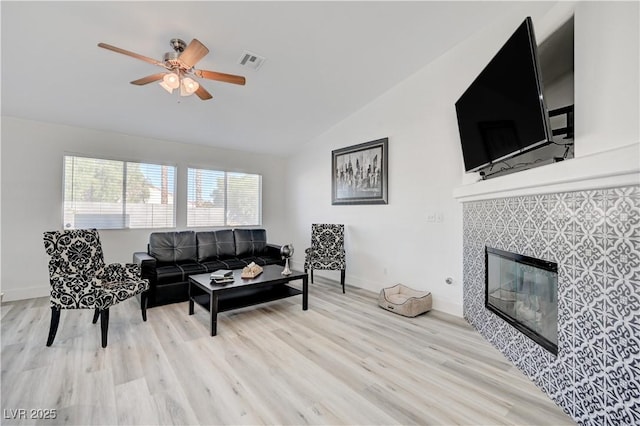 living room featuring a tiled fireplace, ceiling fan, lofted ceiling, and light wood-type flooring