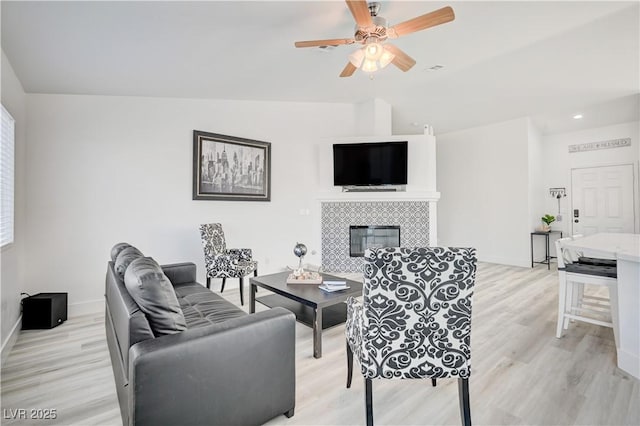 living room with a tile fireplace, light wood-type flooring, and ceiling fan