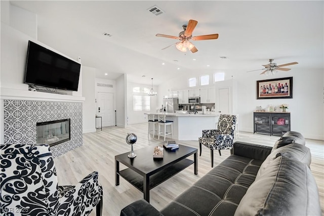 living room with a tiled fireplace, ceiling fan, vaulted ceiling, and light wood-type flooring