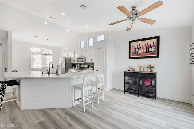 kitchen with pendant lighting, a breakfast bar, white cabinets, vaulted ceiling, and stainless steel appliances