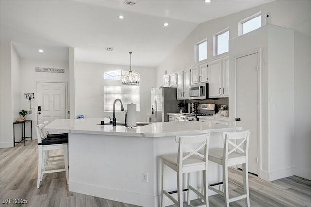 kitchen with white cabinetry, sink, hanging light fixtures, stainless steel appliances, and a kitchen breakfast bar