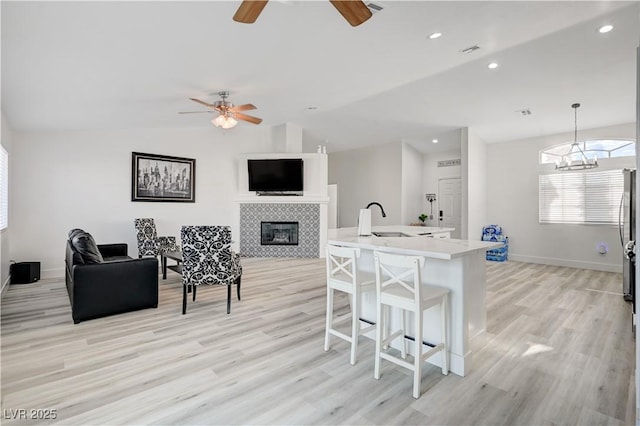 kitchen featuring lofted ceiling, a kitchen breakfast bar, hanging light fixtures, light wood-type flooring, and a tiled fireplace