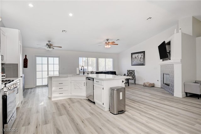 kitchen featuring a tile fireplace, white cabinets, sink, appliances with stainless steel finishes, and light hardwood / wood-style floors