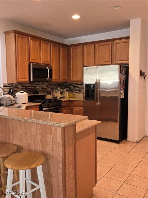 kitchen featuring kitchen peninsula, a kitchen breakfast bar, light stone counters, stainless steel appliances, and light tile patterned floors