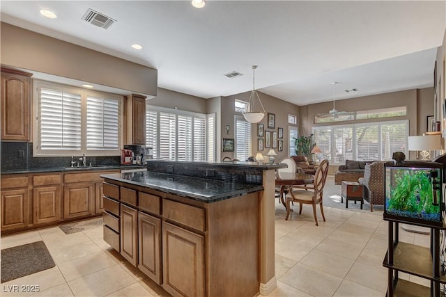 kitchen with a center island, sink, hanging light fixtures, dark stone counters, and light tile patterned flooring