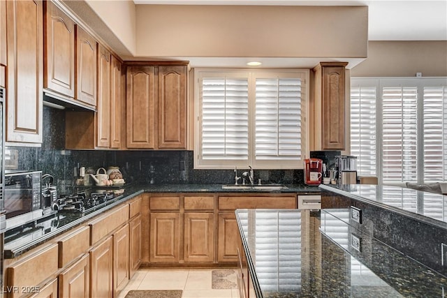 kitchen featuring sink, gas stovetop, tasteful backsplash, dark stone counters, and light tile patterned floors