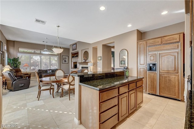 kitchen with paneled fridge, light tile patterned floors, dark stone countertops, a kitchen island, and hanging light fixtures