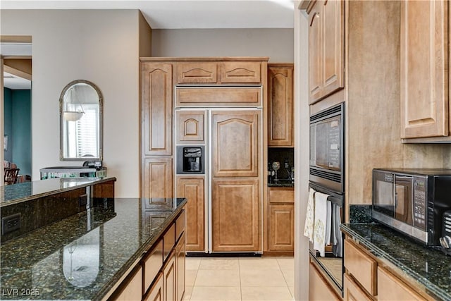 kitchen featuring built in appliances, light tile patterned flooring, and dark stone counters