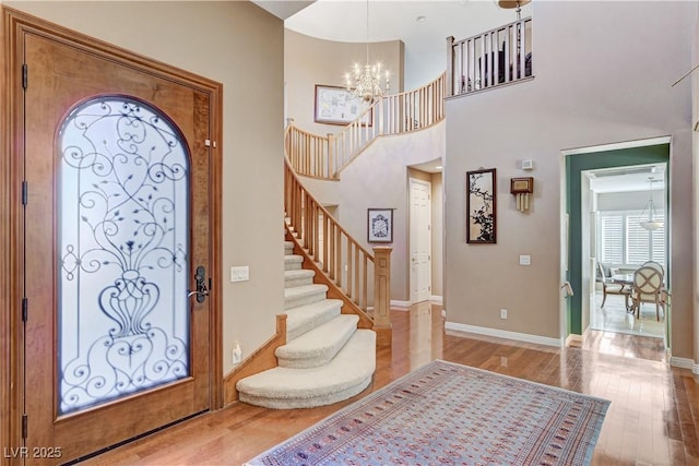 foyer entrance featuring a towering ceiling, a notable chandelier, and light wood-type flooring