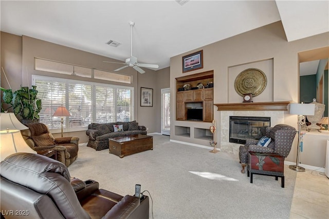 living room featuring built in shelves, ceiling fan, and a tiled fireplace