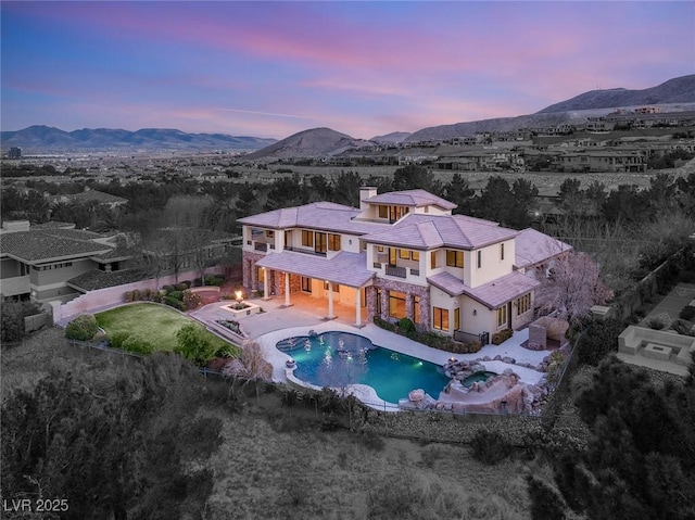 back house at dusk featuring a balcony, a mountain view, and a patio