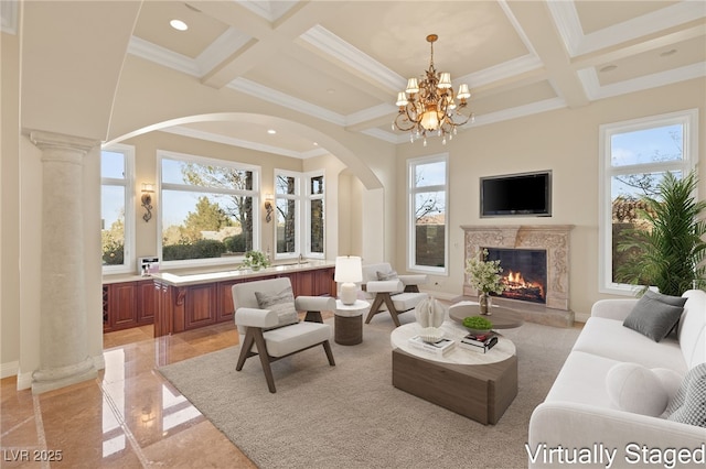 living room featuring ornate columns, coffered ceiling, a notable chandelier, a premium fireplace, and ornamental molding