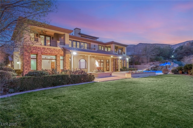 back house at dusk featuring a lawn, a mountain view, and a balcony