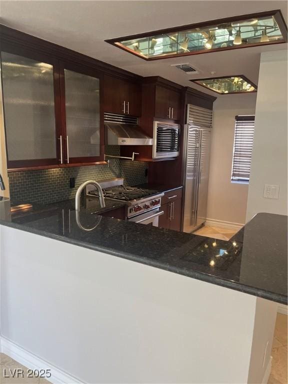 kitchen with under cabinet range hood, visible vents, decorative backsplash, high end appliances, and glass insert cabinets