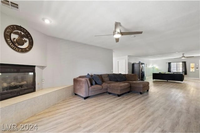 living room with light hardwood / wood-style floors, ceiling fan, and a tiled fireplace