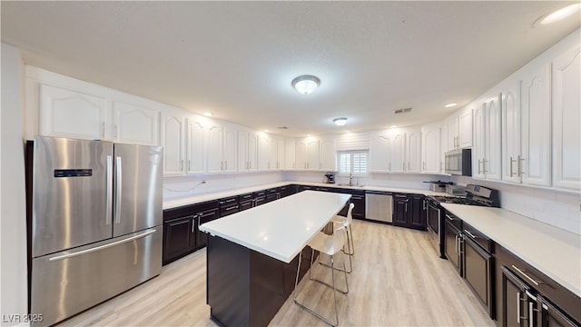 kitchen featuring light wood-type flooring, stainless steel appliances, a center island, white cabinetry, and a breakfast bar area