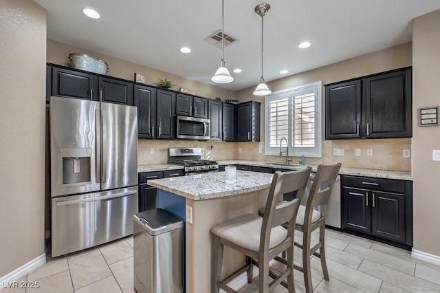 kitchen with light stone countertops, a kitchen island, stainless steel appliances, sink, and hanging light fixtures