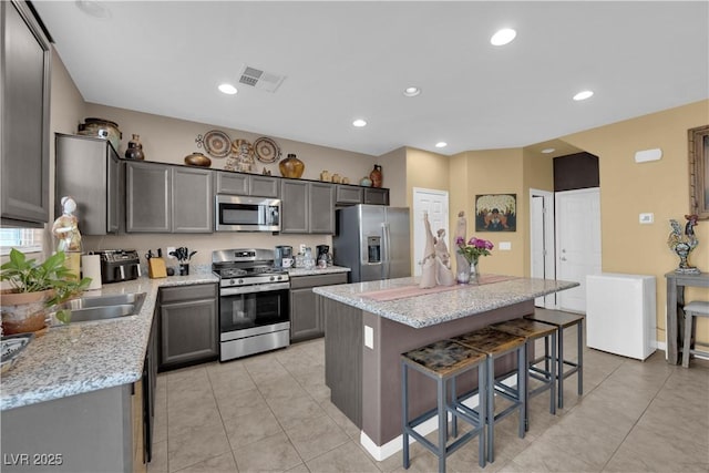 kitchen with light stone countertops, a kitchen breakfast bar, appliances with stainless steel finishes, and a kitchen island