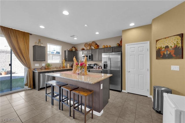 kitchen featuring light tile patterned floors, appliances with stainless steel finishes, a kitchen breakfast bar, light stone countertops, and a center island