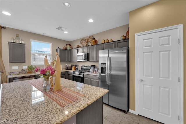 kitchen with light tile patterned floors, light stone counters, stainless steel appliances, and a center island