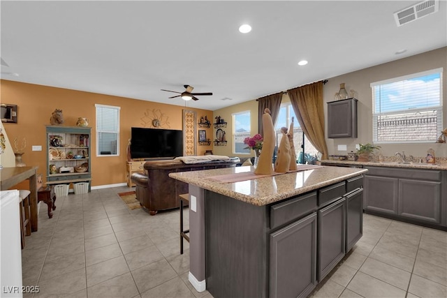 kitchen with ceiling fan, light tile patterned floors, light stone countertops, and a kitchen island