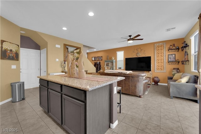 kitchen featuring a kitchen island, ceiling fan, light stone counters, light tile patterned floors, and a breakfast bar area