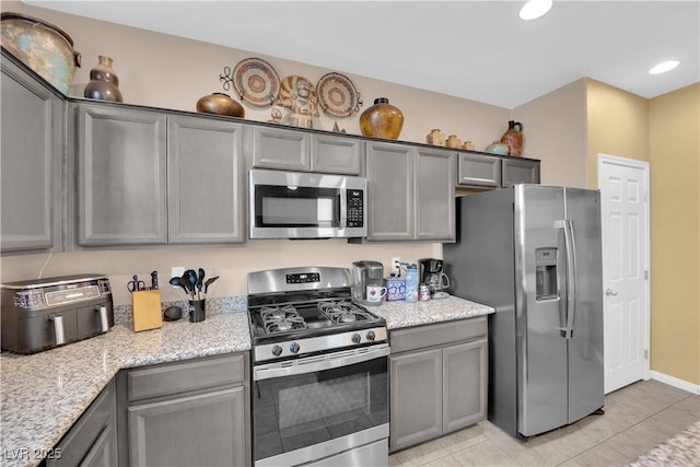 kitchen featuring light stone countertops, light tile patterned floors, appliances with stainless steel finishes, and gray cabinets