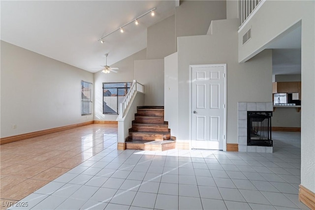 stairs featuring ceiling fan, tile patterned floors, high vaulted ceiling, and a fireplace