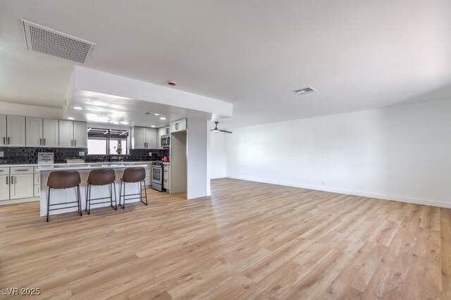 kitchen with gray cabinets, light hardwood / wood-style floors, a kitchen island, a kitchen bar, and stainless steel range