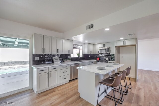 kitchen with appliances with stainless steel finishes, a kitchen bar, light hardwood / wood-style flooring, and a center island