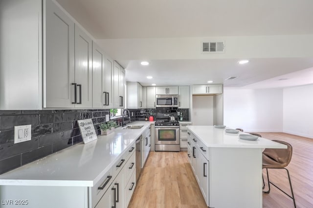 kitchen with appliances with stainless steel finishes, a kitchen island, sink, a breakfast bar, and light hardwood / wood-style flooring