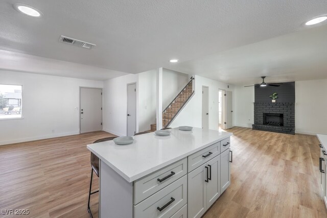 kitchen with light hardwood / wood-style floors, ceiling fan, a breakfast bar area, a fireplace, and a kitchen island