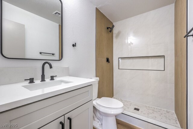 bathroom with toilet, tiled shower, wood-type flooring, and vanity