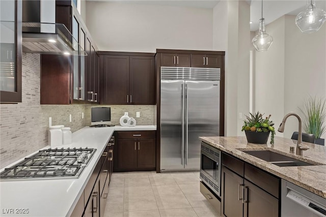 kitchen featuring built in appliances, decorative backsplash, light stone countertops, dark brown cabinetry, and sink