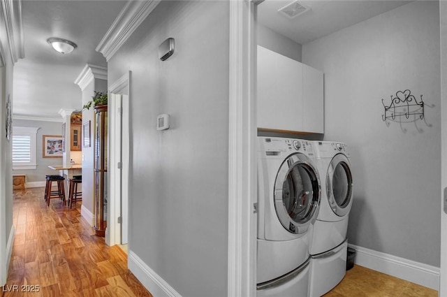 laundry room with separate washer and dryer, light hardwood / wood-style floors, ornamental molding, and cabinets