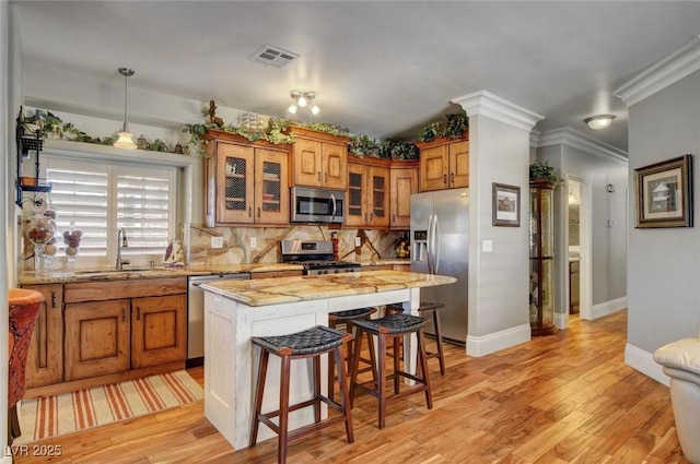 kitchen featuring pendant lighting, sink, stainless steel appliances, a center island, and light wood-type flooring