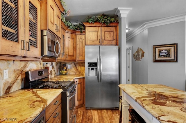 kitchen with crown molding, light wood-type flooring, appliances with stainless steel finishes, light stone countertops, and decorative columns