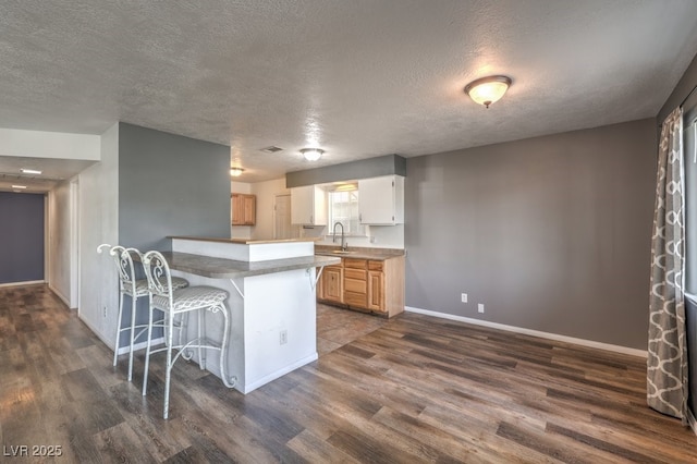 kitchen featuring a breakfast bar, sink, a textured ceiling, dark hardwood / wood-style flooring, and kitchen peninsula