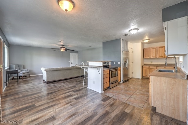 kitchen with sink, a kitchen breakfast bar, wood-type flooring, light brown cabinetry, and appliances with stainless steel finishes