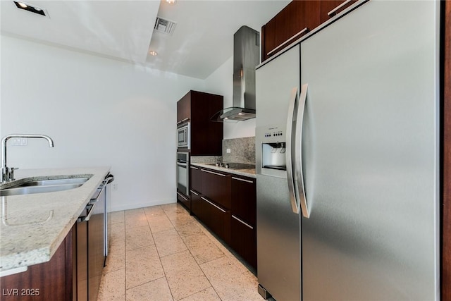 kitchen featuring sink, wall chimney exhaust hood, stainless steel appliances, tasteful backsplash, and a center island with sink