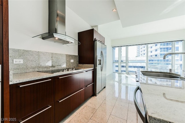 kitchen with black electric stovetop, wall chimney range hood, sink, stainless steel refrigerator with ice dispenser, and light stone countertops