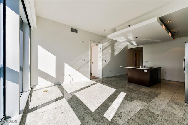 kitchen with dark brown cabinetry, a center island with sink, stainless steel refrigerator, and sink