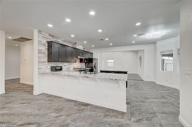 kitchen featuring kitchen peninsula, light stone countertops, backsplash, stainless steel fridge with ice dispenser, and a breakfast bar area