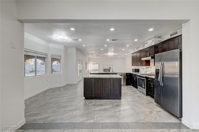 kitchen with dark brown cabinetry, a center island, light stone counters, decorative backsplash, and appliances with stainless steel finishes