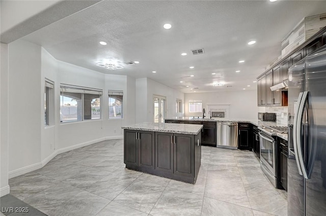 kitchen with light stone countertops, kitchen peninsula, stainless steel appliances, and dark brown cabinetry