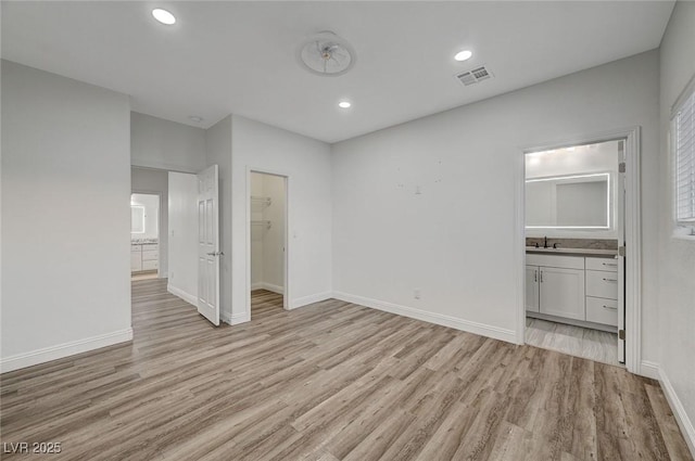 unfurnished bedroom featuring a walk in closet, ensuite bathroom, a closet, and light hardwood / wood-style floors