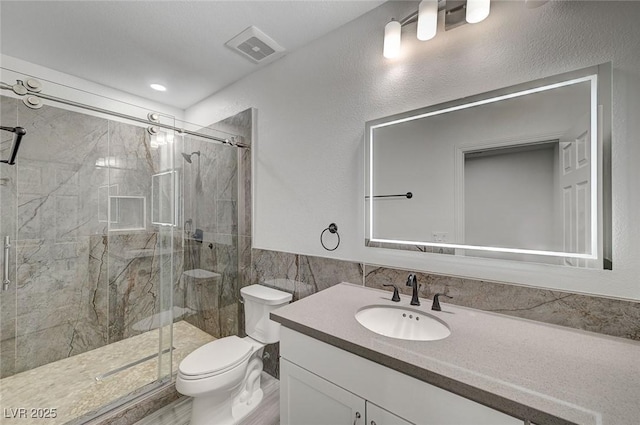 bathroom with an enclosed shower, vanity, toilet, and tile walls