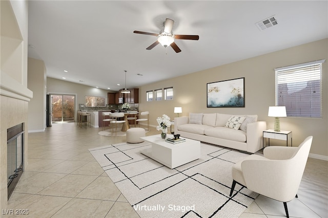 living room featuring ceiling fan, a tile fireplace, vaulted ceiling, and light tile patterned floors