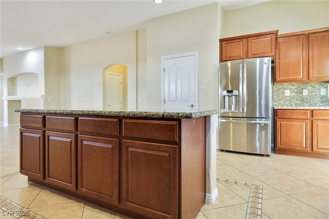 kitchen with light stone countertops, light tile patterned floors, stainless steel fridge, a kitchen island, and decorative backsplash