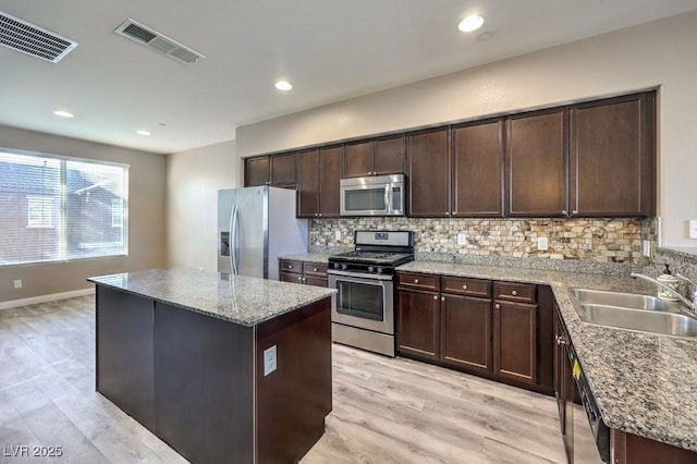 kitchen with sink, a center island, stainless steel appliances, light hardwood / wood-style flooring, and backsplash